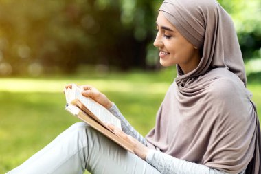Kamu parkında türban okuyan, güzel havanın, manzaranın, fotokopi alanının keyfini çıkaran kızın yakın çekimi.
