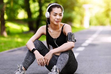 Dışarıdaki eğitimden sonra dinlenin. Kulaklıklı genç Asyalı kadın parkta oturmuş müzik dinliyor başarılı bir çalışmadan sonra dinleniyor ve boşluğu kopyalıyor.