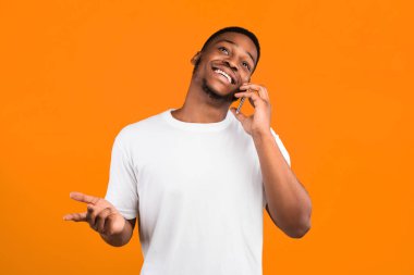 Cep telefonuyla konuşan pozitif Afrikalı adam sarı arka planda duruyor. Stüdyo Çekimi