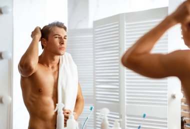 Odaklanmış bir adam aynaya bakıyor. Saçına mum sürüyor. Saç dökülme sorunu var mı diye bakıyor.