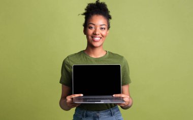 Kullanışlı bir web sitesi. Neşeli afro kız dizüstü bilgisayarını tutuyor, yeşil stüdyo duvarında boş ekran gösteriyor.