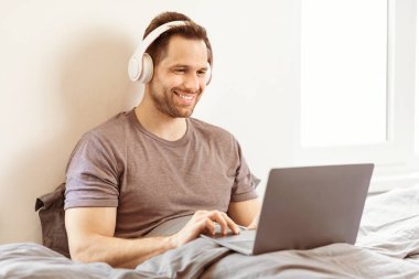 İnternette Film İzle. Laptop kullanan, kulaklık takan, yatak odasında oturup film izleyen bir adam. Hafta sonu Tatili, Eğitici İnternet Web Sitesi Reklamları ve Serbest Yaşam Tarzı
