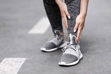 Shin Splints. Açık havada koşarken spor travması geçiren bayan koşucu, ağrı bölgesine dokunuyor, boş alanda kesilmiş görüntü.