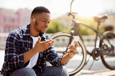 Video Çağrı Konsepti. Şehirdeki internet araması için cep telefonu kullanan siyah adam, güneş ışığı parlaması