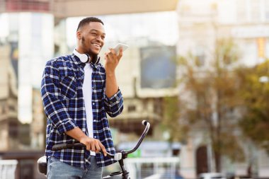 İletişim Konsepti. Cep telefonuyla konuşan Afro-Amerikalı adam hoparlör kullanıyor, alet tutuyor ve bisiklete biniyor.