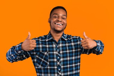 Hoşuma gitti. Siyah Adam Sarı Stüdyo 'nun arka planında duran bir şeyi onaylamak için iki eliyle başparmak hareketi yapıyor.