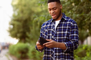 Boş cüzdanı tutan depresif siyahi adam ağzı açık ve üzgün hissediyor, boşluğu kopyala