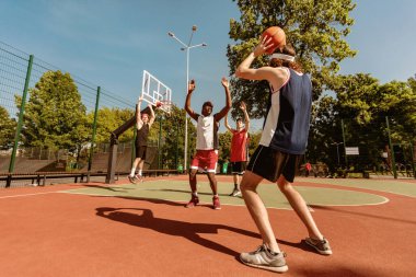 Bir grup genç çok ırklı basketbolcu açık alanda arkadaşça oyun oynuyorlar. Milenyum sporcusu farklı takımlarına top atıyor, dışarıda maç yapıyor.