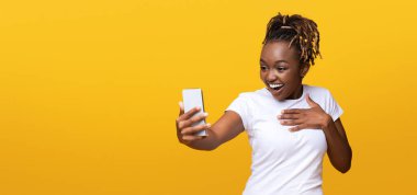 İnternette inanılmaz satışlar. Cep telefonuna bakan ağzı açık, sarı stüdyo arka planı olan, fotokopi alanı olan bir panorama olan siyahi kadın. Heyecanlı Afrikalı Amerikalı kadın elinde akıllı telefon tutuyor.