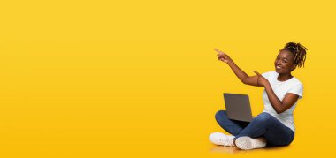 Sarı stüdyo arka planında dizüstü bilgisayarı boş yeri gösteren siyah kız, panorama.