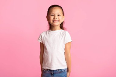 Tatlı gülümseyen Asyalı bir kızın portresi. Kameraya bakıyor ve poz veriyor. Pembe stüdyo duvarında izole edilmiş.