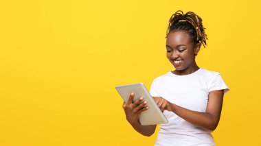 Dijital tabletli güzel Afrikalı kız, yeni uygulama kullanıyor, sarı stüdyo arka planı, kopyalama alanı