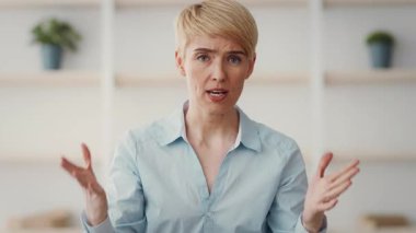 Kısa sarı saçlı bir kadın, anlamlı el hareketleri yaparken bir konuyu tutkuyla tartışır. Parlak oda küçük saksı bitkileriyle dekore edilmiş, hoş bir atmosfer yaratıyor..