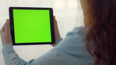 Uzun saçlı bir insan kapalı alanda açık yeşil ekran tableti tutar. Tablet üzerinde duruluyor, yaratıcı projeler veya sunumlar için potansiyel öneriliyor.