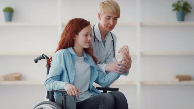 Bir sağlık uzmanı tekerlekli sandalyedeki genç bir kızla temas kuruyor ve terapi seansı sırasında ona destek oluyor. İkisi de konfor ve refahı arttıran bir faaliyete odaklanmış görünüyor..