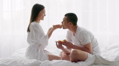 Genç, evli bir çift yataklarında oturmuş pizzanın tadını çıkarırken yatak odalarında eğlenceli bir anı paylaşıyor. Oyuncu etkileşimleri birbirlerine olan sevgilerini ve sevgilerini vurguluyor..