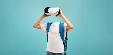 Bir öğrenci canlı mavi bir arkaplan karşısında dururken, bir kulaklık takarak sanal gerçeklik teknolojisine bağlanır..