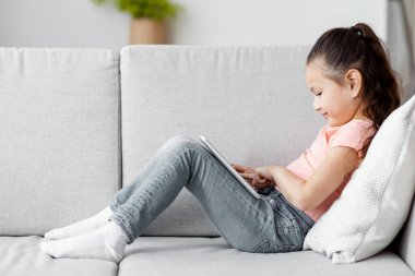 Japon kız dijital tablet bilgisayar kullanıyor. Evdeki kanepede oturmuş çizgi film izliyor. Çocuk ve Gadget. Panorama