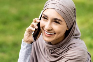 Cep telefonuyla konuşan mutlu genç Arap kadının yakın plan portresi, fotokopi alanı, park arka planı