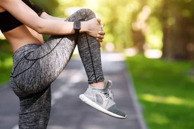 Kadın sporcu sabah koşusuna hazırlanıyor. Parkta koşuyor, bacak kaslarını esnetiyor, boş alanlı kesilmiş görüntü. yan görünüm