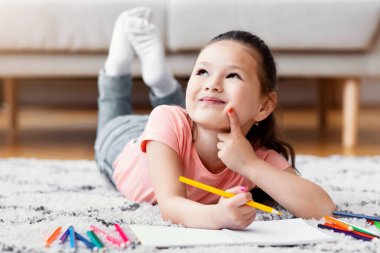 Hafta sonları evde yerde yatan küçük Çinli bir kız eskiz çiziyor. Çocukların Yaratıcılık ve Yetenek Konsepti