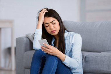 Onun aramasını bekliyorum. Mutsuz Koreli kadın oturma odasında üzgün bir ifadeyle otururken akıllı telefon ekranına bakıyor, kötü mesaj alıyor, depresyon geçiriyor, boş alan arıyor.