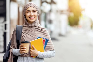 Tesettürlü neşeli kız üniversiteden önce sokakta sabah kahvesi içiyor.
