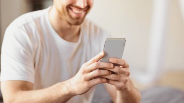 Tanımlanamayan Gülümseyen Adam Akıllı Telefon Cep Telefonu Uygulamasını Evdeki Yatak Odasında Otururken Telefona Odaklan. Sosyal medya uygulaması konseptiyle cep telefonunda mesajlaşan adam. Kırpılmış, Seçici Odaklanma, Panorama