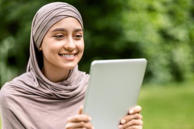 Halka açık parkta dijital tablet kullanan neşeli Arap kızın sosyal medyasını kontrol edip, boşluğu kopyalaması