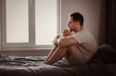 Endişe kavramı. Depresyondaki adam, evde, yatakta oturan sorunları düşünüyor. Metin için Boş Alan
