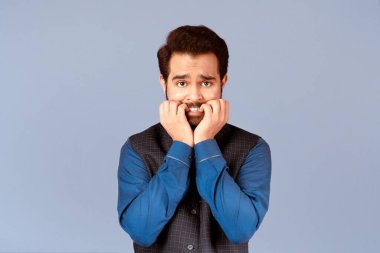 Korkmuş Hintli adam, leylak arkaplanı yüzünden panik içinde tırnaklarını yiyor.