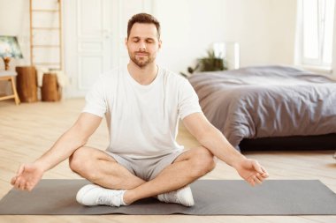 Sakin ol. Zen-benzeri bir adam, Lotus pozisyonunda oturmuş evde dinlenirken gözleri kapalı meditasyon yapıyor. Sabah Yogası, Rahatlama Egzersizi. Metin için Boşluk