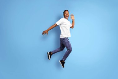 Afro-Amerikalı Adam Mavi Arkaplan 'ın üzerinde bir şeyin reklamını yaparak havadan atlıyor. Stüdyo Çekimi, Boş Alan