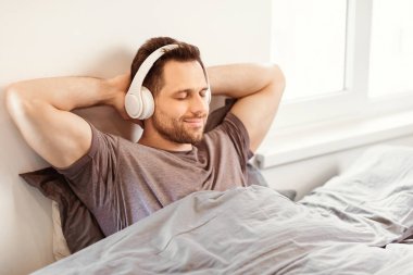 Evde yatağında gözleri kapalı oturan ve kulaklık takan müzik dinleyen rahat bir adam. Hafta sonu Tatil Konsepti