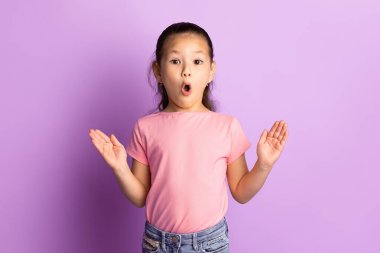 Şaşırmış, ağzı açık, ellerini heyecan içinde açan, pastel mor stüdyo duvarında izole edilmiş Asyalı bir kız.