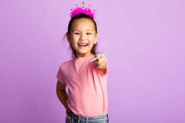 Küçük Prenses. Kafasına taç takmış yakışıklı Asyalı çocuk sihirli çubuğu kameraya doğrultuyor, mor renkli stüdyo duvarı, fotokopi odası.