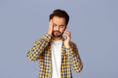 Baş ağrısı ya da depresyonu olan genç Hintli adam leylak arkaplanı üzerinden akıllı telefonla konuşuyor.