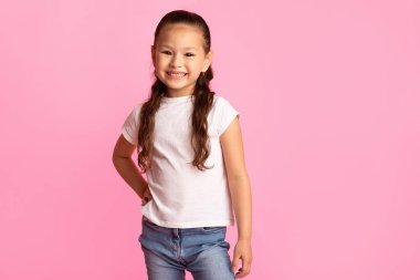 Küçük Model. Kameraya poz veren kendine güvenen Asyalı kız, el ele tutuşuyor, pembe stüdyo duvarı, fotokopi odası.