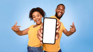 Bu yeni mobil uygulamayı kullan. Neşeli Afro-Amerikan çift boş beyaz ekranla akıllı telefonu işaret ediyor, web sitenizin reklamını yapıyorlar, maket yapıyorlar. Seçici odaklanma. Pankart tasarımı
