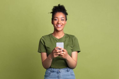 Harika bir uygulama. Gülümseyen Afrikalı kadın yeşil stüdyo arka planında akıllı telefon kullanıyor ve kameraya bakıyor.