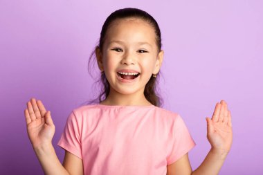 Vay canına. Heyecanlı Asyalı çocuğun yakından çekilmiş portresi gülümseyen ve el kaldıran, Pastel mor stüdyo duvarında izole edilmiş.