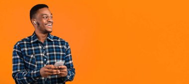 Smartphone ve Kulaklıklı Mutlu Afrikalı Adam Sarı Arkaplanda Müzik veya Podcast Dinliyor. Stüdyo Çekimi