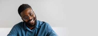 Genç bir Afrikalı Amerikalı işadamı ofis masasında otururken kendinden emin bir şekilde gülümsüyor. Girişimci ruhunu somutlaştırıyor, kariyerindeki başarıyı ve kararlılığı yansıtıyor, boşluğu kopyalıyor.