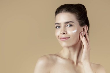 Güzel kız bej arka planda yüzüne nemlendirici krem sürmüş.