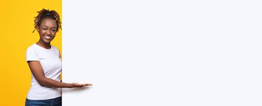 Sarı arka plan, panorama üzerinde reklam için beyaz boş tahtası olan gülümseyen siyah kadın.