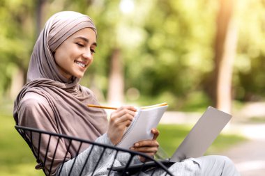 Zeki Arap kız halka açık bir parkta ders çalışıyor, dizüstü bilgisayar kullanıyor, notlar alıyor, sınavlardan önce hazırlanıyor, boşluk