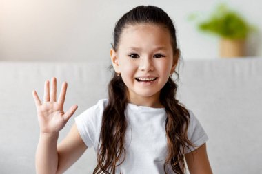 Hoş geldiniz. Sevimli Asyalı kız el sallıyor. Kameraya gülümsüyor. Evdeki koltukta oturuyor.