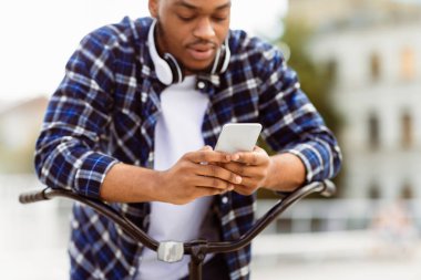 Afrika kökenli Amerikalı bir adamın akıllı telefondan SMS mesajlaşması bisikletinin sapına yaslanması, seçici bir şekilde odaklanması.
