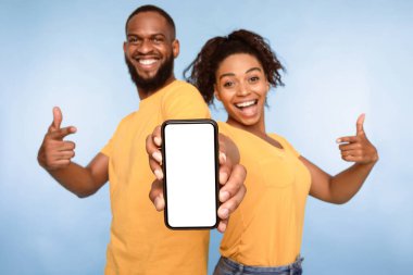 Bu yeni uygulamayı kullan. Neşeli Afrikalı Amerikalı çift boş ekranlı akıllı telefonu işaret ediyor, mobil uygulama öneriyorlar, web sitenizi tanıtıyorlar, tasarım için maket yapıyorlar. Seçici odak