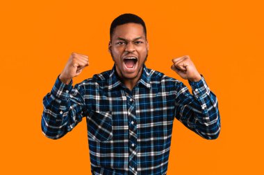 Duygusal Afrikalı Amerikalı Adam Sarı Arkaplan 'ın üzerinde duran kameraya bakarak yüksek sesle titreyen yumruklar atıyor. Stüdyo Çekimi